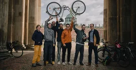 Gruppe von Menschen steht zwischen Säulen, einer übergibt ihnen einen Pokal