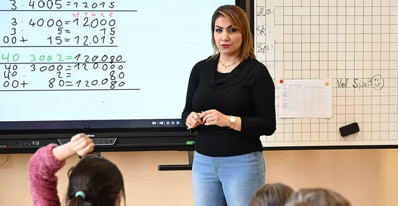 Entisar Karkokli vor Tafel im Klassenraum.