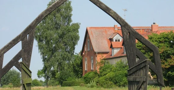 Natur mit einem Haus, einem Holzbogen und einem Storch