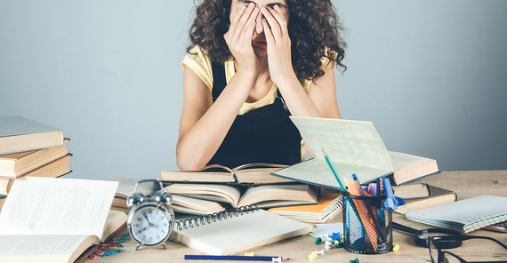 Stressed student with books scattered around her desk.