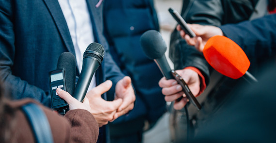 Auf dem Bild sind Mikrofone vor einer Person im Anzug zu sehen.