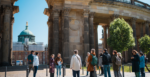 Gruppe von Menschen steht bei der Kolonnade des Neuen Palais