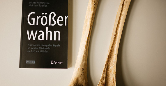 Close-up of the book "Größenwahn". Next to it are two halves of a bone (thigh bone) cut lengthwise.