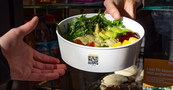 Hand überreicht einer anderen Hand Essen in einer Relevo-Schale.