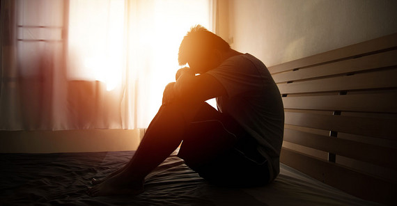 Mann sitzt auf dem Bett, den Kopf an die Knie gesenkt. Das Bild ist von AdobeStock/kwanchaift.