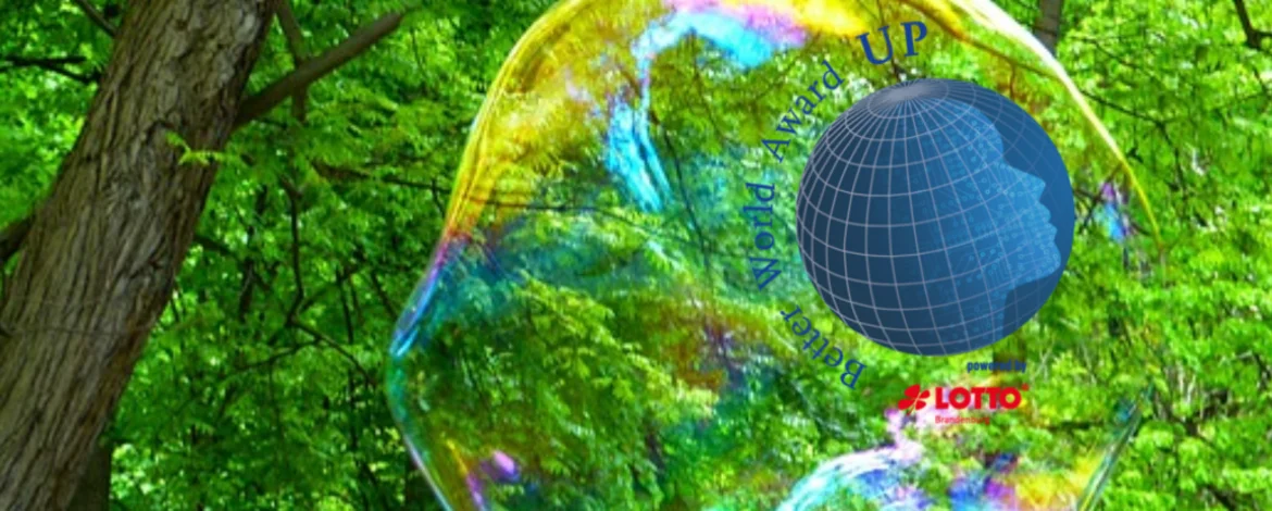 Ein Globus umgeben mit Schrift "Better World Award" und "powered by Lotto Brandenburg". Im Bildhintergrund das grüne Laubdach eines Waldes und große Seifenblasen. - 