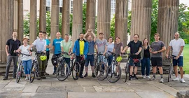 Eine große Gruppe von Menschen posiert breit aufgestellt, teils mit Fahrrädern, für ein Gruppenfoto.
