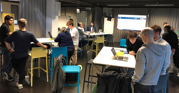 People are standing at tables in a room and talking to each other.