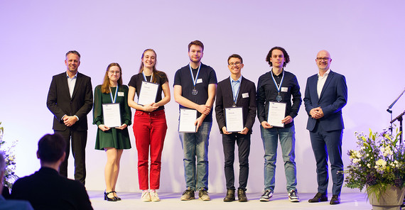 Gruppe von sechs Menschen posiert mit urkunden auf einer Bühne