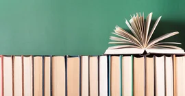 Bücher in einem Regal nebeneinander mit aufgeklappten Buch obenauf.