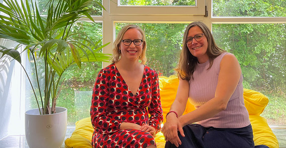 Zwei Frauen sitzen auf einer Fensterbank und schauen in die Kamera