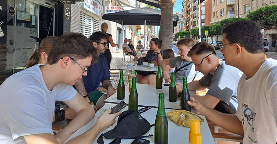 Die Studierenden sitzen an einem Tisch in einem Straßencafé und genießen kühle Getränke.