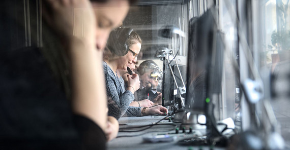 Reihe von jungen Menschen, die an einem langen Tisch vor PCs sitzen und arbeiten