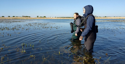 Two cheerful students in waders, knee-deep in the flooded study area.