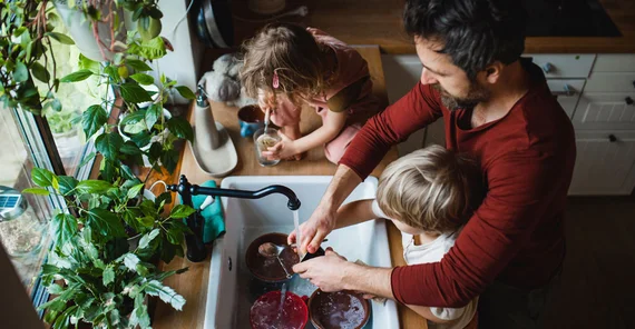Mann mit zwei Kindern steht in der Küche und wäscht ab. Das Foto ist von AdobeStock/Halfpoint.