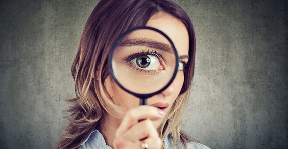 Portrait of a young woman holding up a magnifying glass to her eye