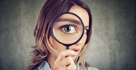 Portrait of a young woman holding up a magnifying glass to her eye