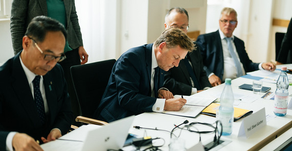 mehrere Männer, die an einem Tisch etwas unterschreiben