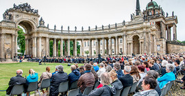 Gäste sitzen vor den Kolonnaden und verfolgen das Programm